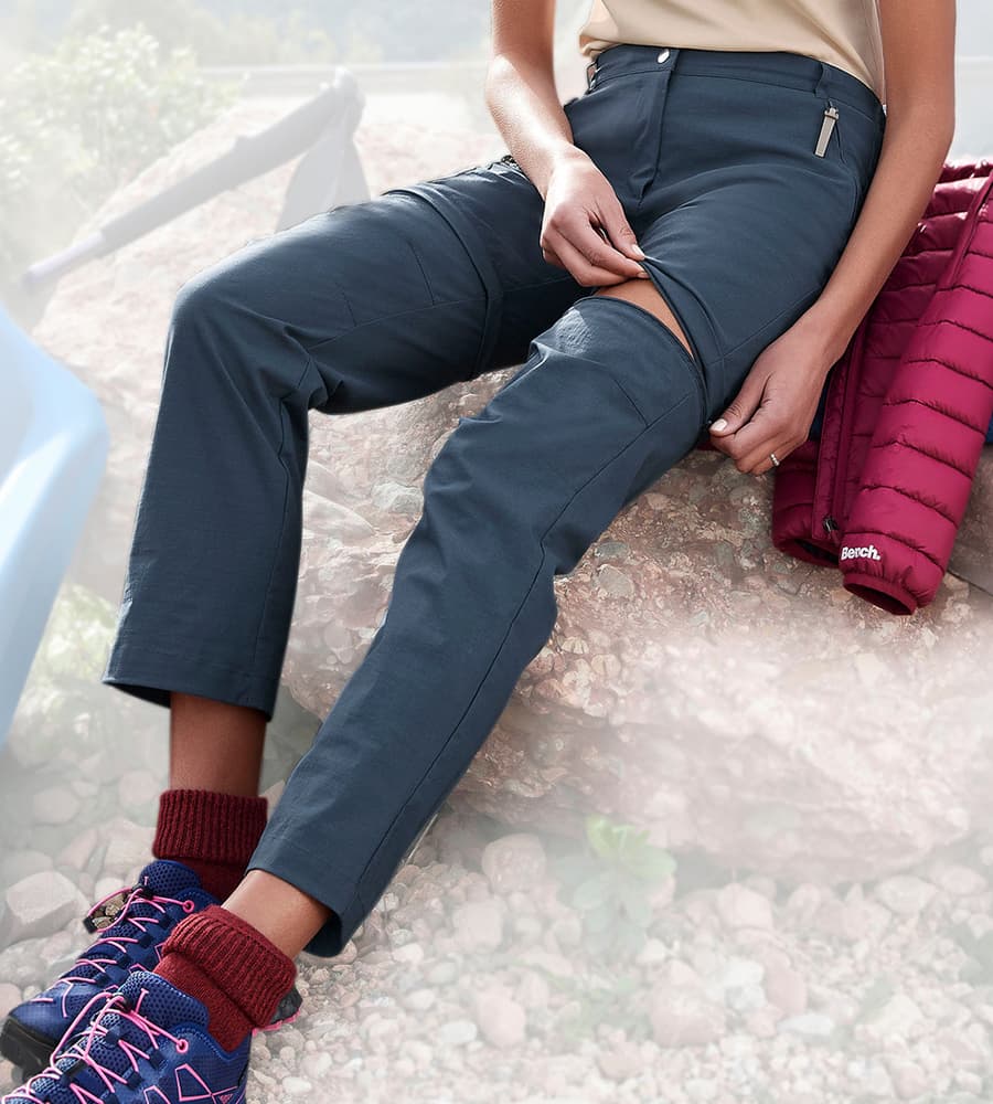 Frau im Gelände öffnet Reißverschluss an der Wanderhose, um sie in eine kurze Hose zu verwandeln