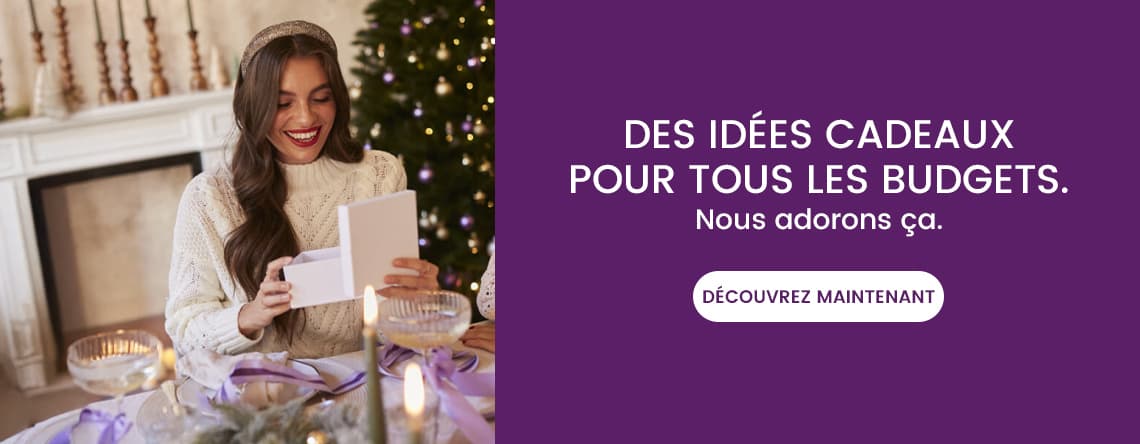 Des idées cadeaux pour tous les budgets. Nous adorons ça. Femme ouvrant un cadeau, assise près d'un sapin de Noël décoré.