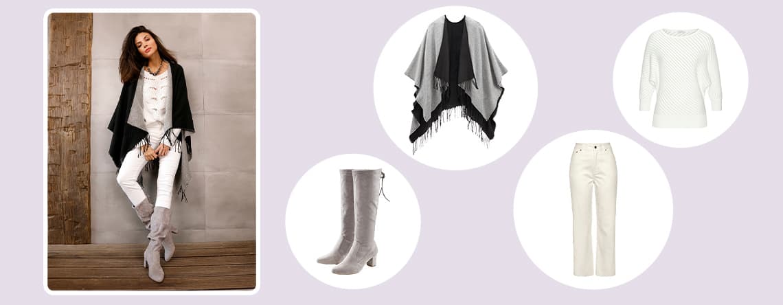 Ensemble mode avec poncho noir, pull blanc texturé, pantalon blanc et bottes grises, porté par une femme debout contre un mur