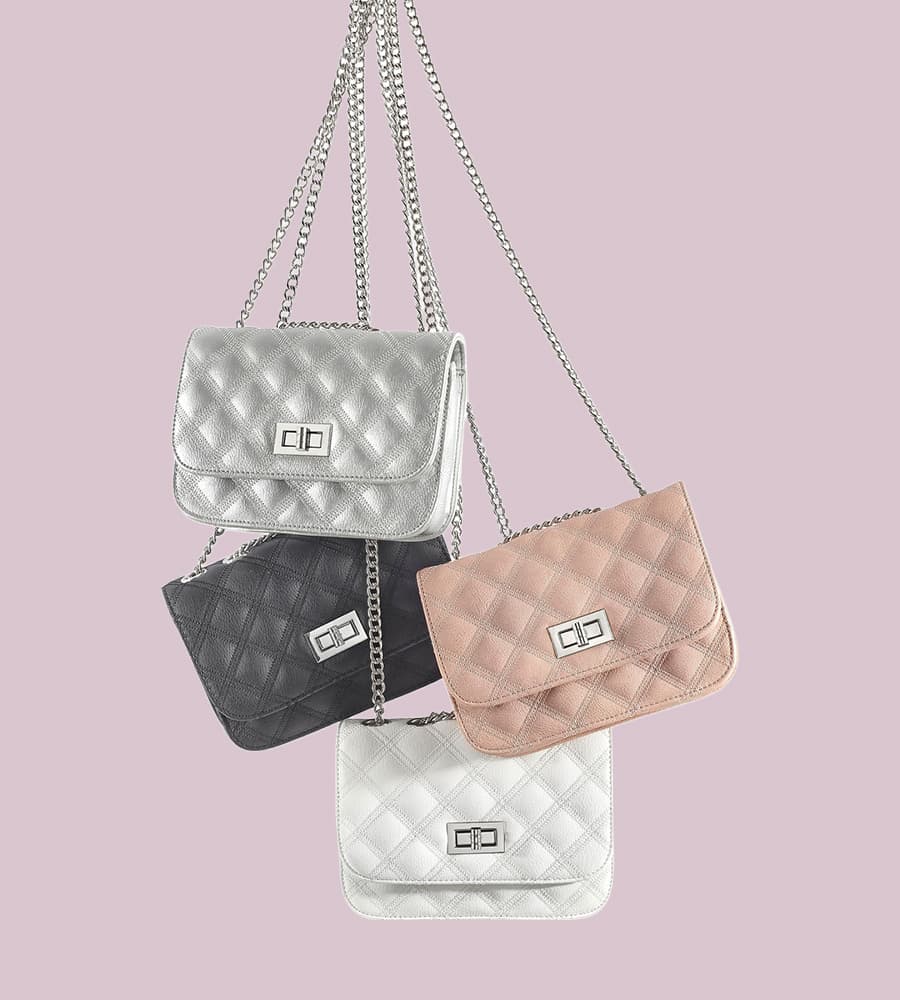 Vier gesteppte Handtaschen in Silber, Schwarz, Rosa und Weiß hängen an silbernen Ketten vor einem rosa Hintergrund