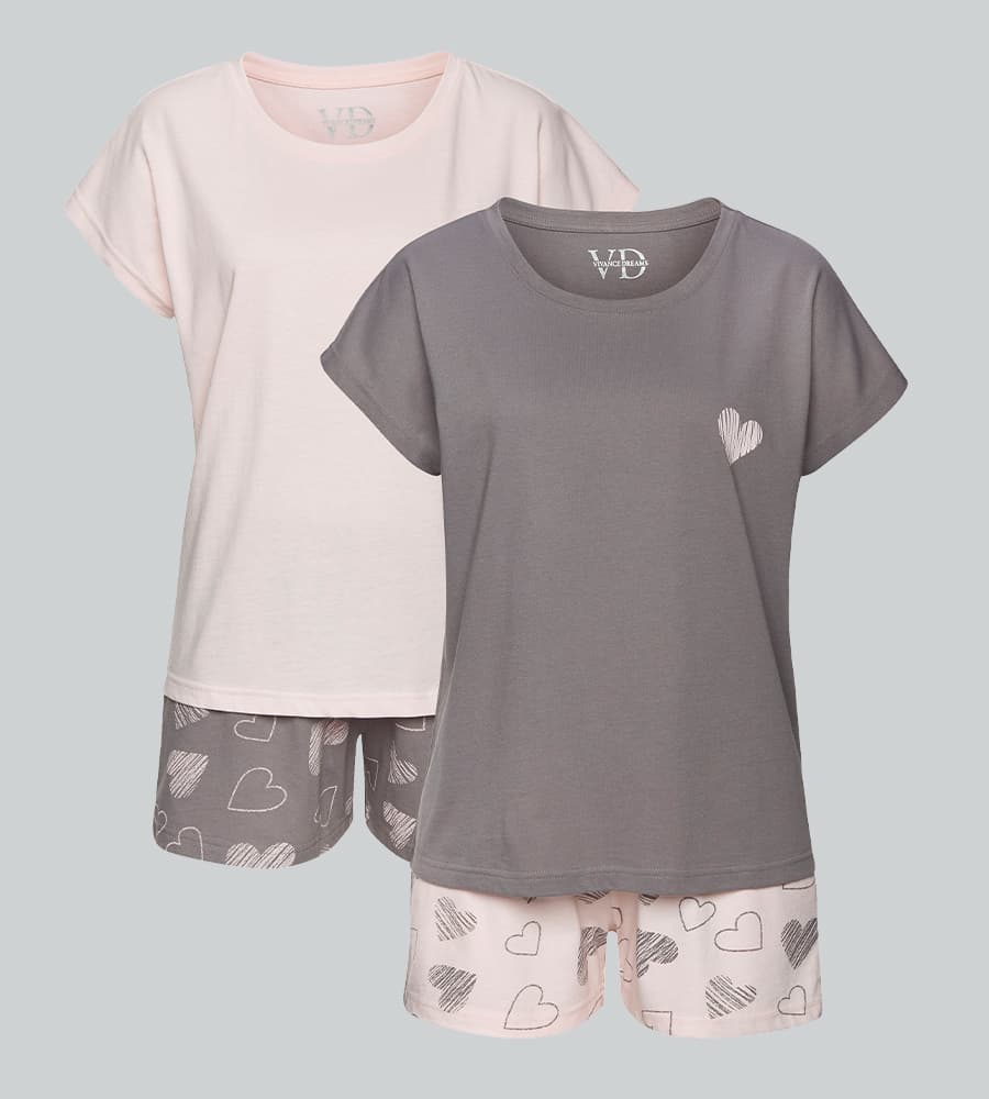 Zwei kurze Damenpyjamas, grau und rosé, mit Herzmotiv auf Shirt und Shorts vor hellem Hintergrund