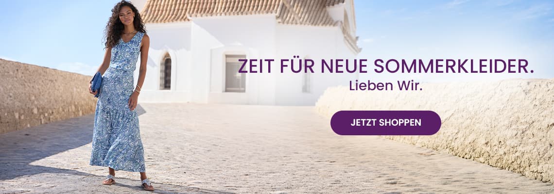 Zeit für neue Sommerkleider – Frau in langem gemustertem Kleid steht auf sonnigem Platz vor weißem Gebäude